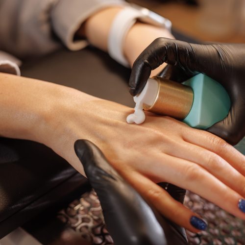 manicurist applies cream to client's hands for hand care in beauty salon